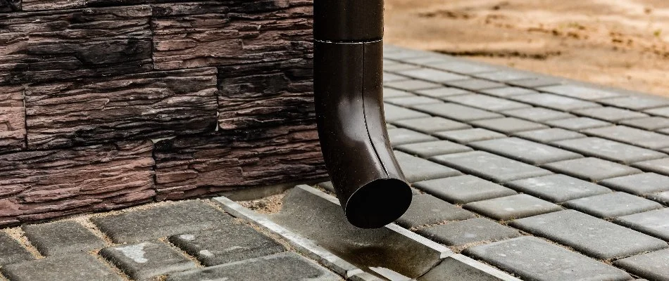 A brown downspout in Lititz, PA, over concrete pavers.